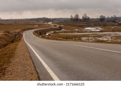 Low angle photo of tarmac curvy road at vintage brown meadows at early spring. Melancholic winding drive at countryside from left. Twisty gray asphalt path near Ergli, Latvia during rainy day.  - Shutterstock ID 2171666125