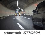 A low angle point of view shot from a moving vehicle inside a modern underground concrete tunnel, showing a gray passenger van and a blurry truck ahead with motion blur.