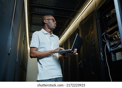 Low angle portrait of African American man managing server network and using laptop, IT technician