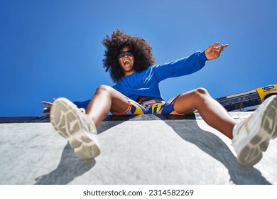 Low angle portrait carefree young woman with arms outstretched cheering at edge of sunny sports ramp