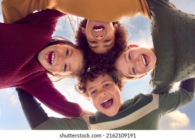 Low Angle Portrait Of Children Having Fun Playing Outdoors Linking Arms Looking Down Into Camera