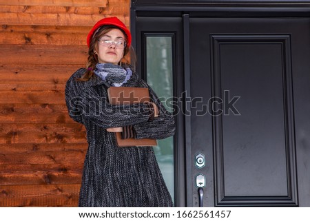 low angle portrait of construction inspector woman with confident look standing outdoor next to a house entrance and holding a clipboard.