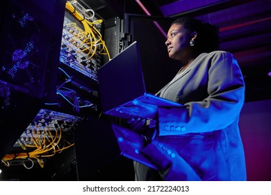 Low angle portrait of female network engineer setting up servers in data center lit by neon - Powered by Shutterstock