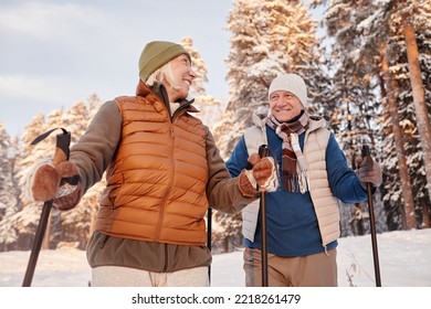 Low angle portrait of happy senior couple walking with poles in winter forest and smiling - Powered by Shutterstock