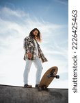 Low angle portrait of long haired man holding his skateboard with his foot on the pool edge