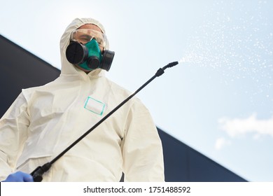 Low angle portrait of male worker wearing hazmat suit holding disinfection gear spraying chemicals outdoors while standing against sky background, copy space - Powered by Shutterstock