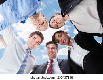 Low Angle Portrait Of Multiethnic Business People Forming Huddle Against Sky