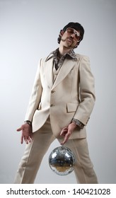 Low Angle Portrait Of A Retro Man In A 1970s Leisure Suit And Sunglasses Holding A Disco Ball - Mirror Ball Between His Legs