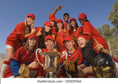 Low Angle Portrait Of Successful Female Softball Team And Coach With Trophy Celebrating Against Blue Sky