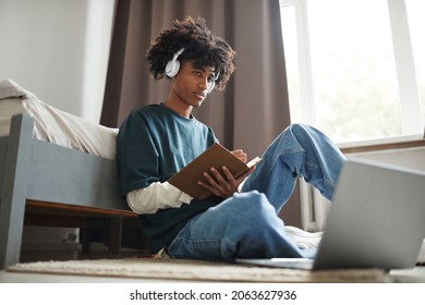 Low Angle Portrait Of Teenage African-American Student Sitting On Floor At Home Or In College Dorm And Studying , Copy Space