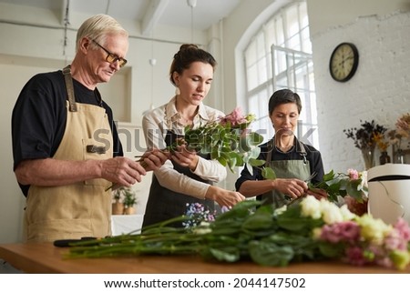 Low angle portrait of three creative florists arraigning flower compositions in workshop
