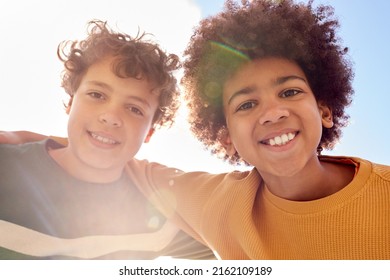 Low Angle Portrait Of Two Boys Having Fun Playing Outdoors Looking Down Into Camera With Lens Flare