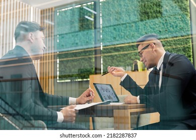 Low Angle Portrait Of Two Successful Business People Wearing Suits During Meeting In Conference Room Behind Glass Wall