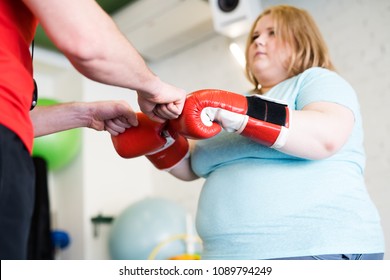 Low angle portrait of young obese woman fist bumping with personal fitness coach during training in gym, copy space