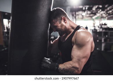 Low angle portrait of young tired sports man leaning on punching bag during boxing practice in fight club - Powered by Shutterstock