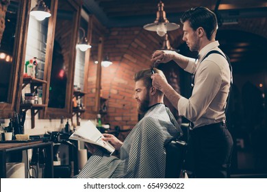 Low angle profile view of red bearded stylish barber shop client, which is getting his perfect  haircut from a classy dressed stylist, reading the magazine and waiting for result - Powered by Shutterstock