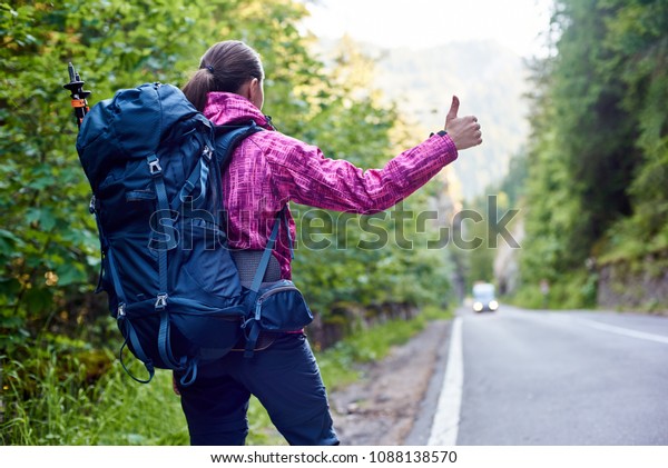 Low angle rear view shot of a female hiker with a\
backpack hailing calling catching a car on Bicaz Canyon road\
copyspace beauty nature wilderness exploring ecology environment\
active lifestyle trip.