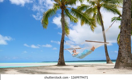 LOW ANGLE: Relaxed tourist girl sleeping in a hammock under the lush palm trees on the breathtaking sandy beach on remote paradise island in the Pacific. Young woman swaying in hammock during vacation - Powered by Shutterstock