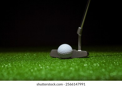 Low angle selective focus of golf ball and putter on a green with black background