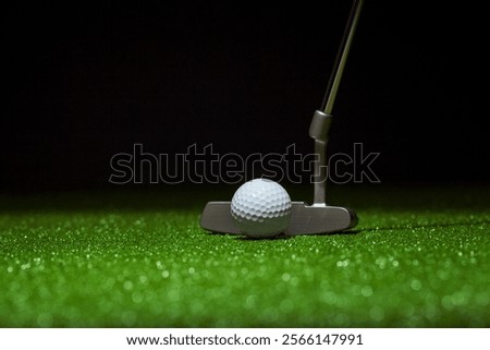 Low angle selective focus of golf ball and putter on a green with black background