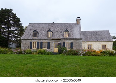 Low Angle Selective Focus View Of Beautiful French-style Patrimonial Stone House With Wooden Extension, Blue Shutters And Cedar Shingles Roof In A Rural Village, Neuville, Quebec, Canada