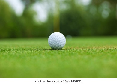 Low angle selective focus view of a golf ball on a green with the flag stick behind