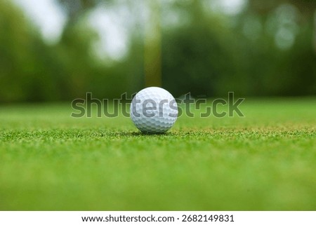 Low angle selective focus view of a golf ball on a green with the flag stick behind