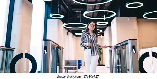 Low angle of serious businesswoman in striped shirt and white pants scanning smartphone at entrance gate while leaving contemporary office building - Powered by Shutterstock