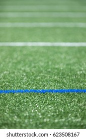 Low angle shallow depth of field parallel geometric blue and white painted yard lines on new artificial green grass turf athletic stadium