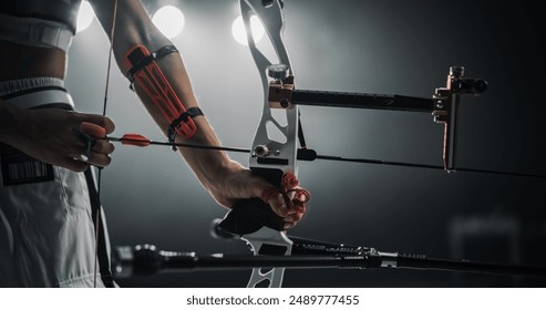 Low Angle Shot Of an Anonymous Female Archer Holding a Modern Compound Bow, Aiming at a Target. Young Athlete Drawing the Arrow in a Stadium Competition or a Dark Studio for Advertising - Powered by Shutterstock