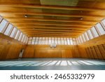 Low angle shot of a basketball court with no people and with a hoot. Wide empty space of a high school sports hall with big windows all around, wooden ceiling and without people. Copy space.