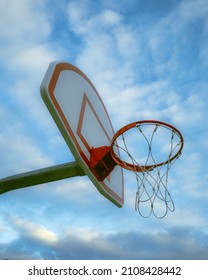 A low angle shot of a basketball hoop under a blue cloudy sky and sunlight