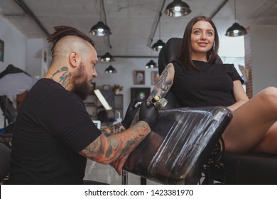 Low angle shot of a beautiful young woman getting arm sleeve tattoo by professional tattooer. Tattoo artist working at his salon, tattooing lovely female customer