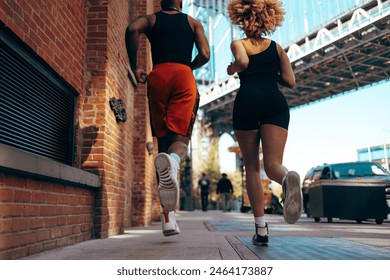 Low angle shot from behind of two African-American joggers on the street beneath the Brooklyn bridge.