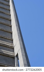 A low angle shot captures the sharp vertical corner and repetitive horizontal slabs of a grey brutalist concrete building against a clear blue sky