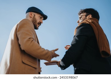 A low angle shot captures two men in a heated discussion with expressive gestures, set against a stark blue sky backdrop.