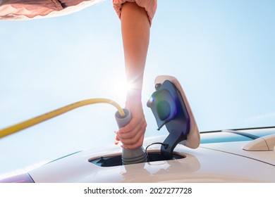 Low angle shot of a Caucasian woman opening an electric car charging socket cap and plugging in a charger