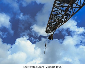 Low angle shot of a construction crane boom against a dramatic blue sky with white clouds