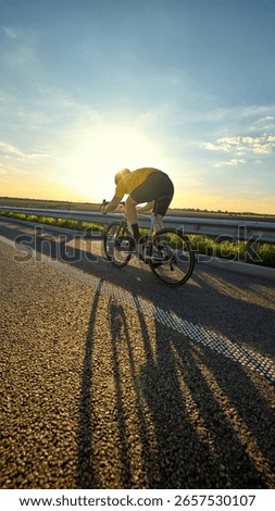 Low angle shot of cyclist creating long shadow under warm sun, pedaling with power in motion. Concept of energy, movement, sport vibe, motivation, effort, and sunrise training journey.