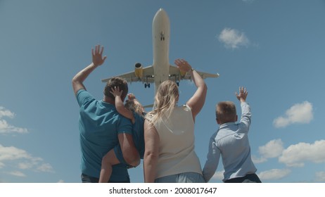 Low Angle Shot Of Family With Kids Waving Hands To The Arriving Airliner Flying Over Head