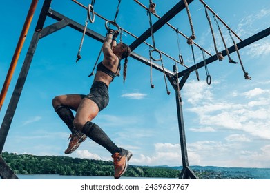 Low angle shot of a female participating in an obstacle course race outdoor while passing the suspensions obstacle. Wearing active wear, trail running shoes with good grip and gloves for protection. - Powered by Shutterstock