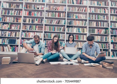 Low angle shot of four international clever bookworms students in the library studying, sitting with crossed legs on the floor together, using books and devices, huge book shelves background - Powered by Shutterstock