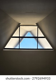 Low angle shot of a futuristic triangular skylight window with clear blue sky view, minimalist architectural geometric design