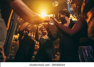 Low angle shot of group of friends enjoying drinks at bar together. Young people at nightclub toasting cocktails.