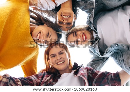 Low angle shot of a group of young women huddling outdoors. Female friends standing in a circle looking at camera and smiling.