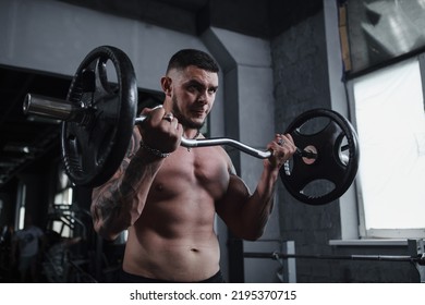 Low angle shot of a handsome ripped tattooed male athlete working out with barbell, looking focused - Shutterstock ID 2195370715