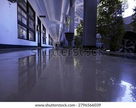 Low angle shot of a long empty outdoor office corridor with clean glossy floor showing perfect symmetry reflection. Architecture building hallway with potted plants