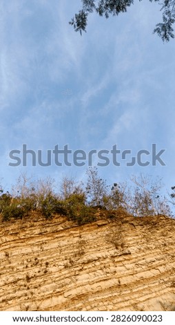 Low angle shot looking up towards a layered rocky cliff edge and bright blue sky.
