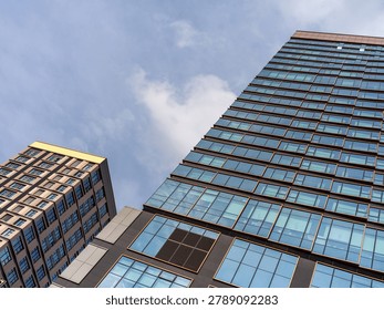 Low angle shot looking up at two modern glass and bronze-framed office buildings against a blue sky with soft white clouds. The image captures commercial expansion, financial strength, and futuristic architecture.