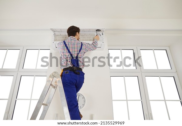 Low angle shot of male mechanic or repairman\
stand on ladder fix air condition device. Man electrician or\
engineer repair conditioner at client house. Good quality\
maintenance technician\
service.